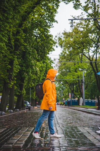 Hombre cruzando la calle con impermeable amarillo clima nublado