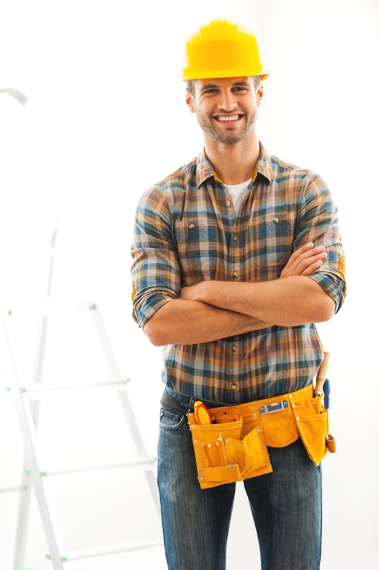 Hombre para cualquier trabajo. Alegre joven constructor manteniendo los brazos cruzados y sonriendo mientras está de pie en el interior