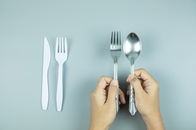 Hombre con cuchara de acero inoxidable y tenedor sobre herramienta de plástico blanco. Protección del medio ambiente, cero residuos, reutilizable, decir no plástico, concepto del día mundial del medio ambiente y del día de la tierra