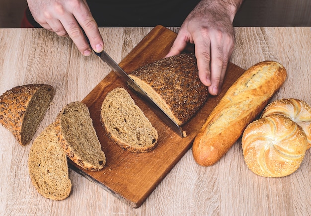 Un hombre con un cuchillo corta el pan en una tabla de madera. Baguettes francesas. Diferentes razas sobre fondo de madera.