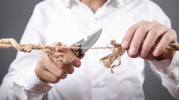 Hombre con cuchillo cortando cuerda deshilachada. Riesgo