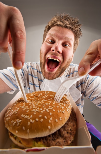 Hombre con cuchillo y tenedor comiendo hamburguesa