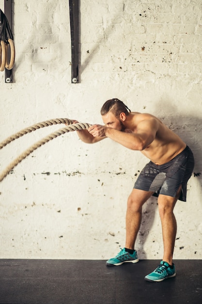 Hombre con cuerdas de batalla haciendo ejercicio en el gimnasio