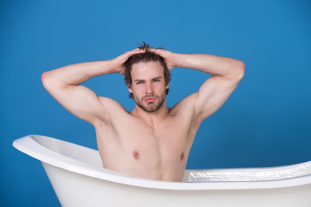 Hombre con cuerpo musculoso sentado en la bañera blanca
