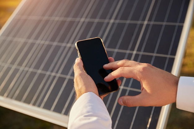 Hombre de cultivo usando un teléfono inteligente en una granja solar