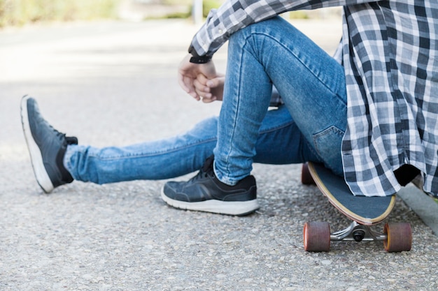 Hombre de cultivos en jeans sentado en longboard