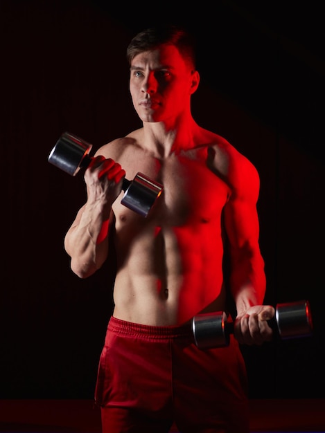 Hombre culturista levantando pesas trabajando enfocado en sus bíceps frente al espejo en el gimnasio Atleta sosteniendo dos pesas mostrando venas tensas en las manos tripas de burbujas