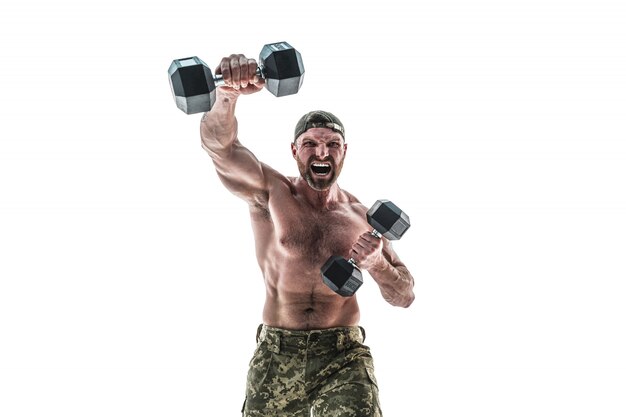 Hombre culturista musculoso atleta en pantalones de camuflaje con un torso desnudo golpeando con pesas como boxeador