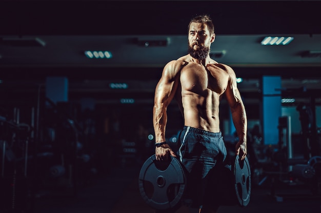 Foto hombre culturista musculoso atleta posando con pesas en el gimnasio.