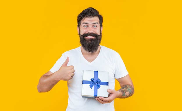 Hombre de cumpleaños sosteniendo caja de regalo pulgar arriba hombre barbudo con caja de regalo en estudio