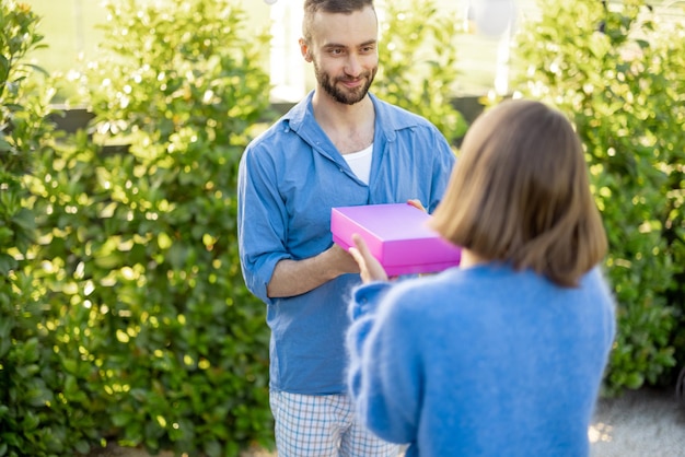 El hombre le da un regalo en una caja rosa a su mujer celebrando al aire libre