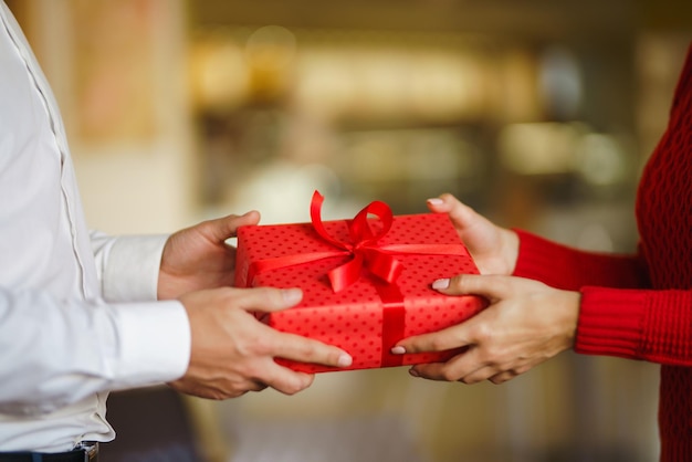 El hombre le da a su mujer una caja de regalo con cinta roja Las manos del hombre le dan una caja de regalo sorpresa para la niña