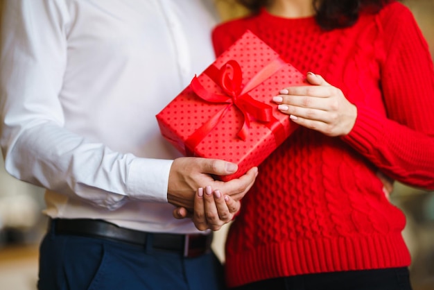 El hombre le da a su mujer una caja de regalo con cinta roja Las manos del hombre le dan una caja de regalo sorpresa para la niña