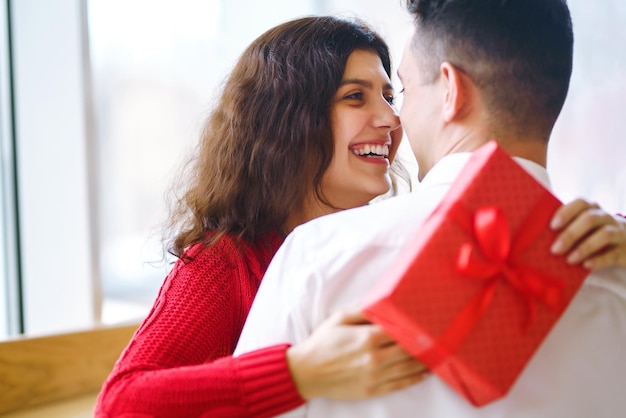 El hombre le da a su mujer una caja de regalo con una cinta roja Una pareja amorosa se abraza, celebrando el Día de San Valentín