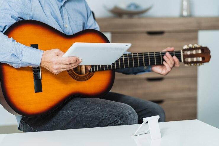 Foto hombre dando una clase de guitarra en línea con la tableta, está revisando la lección