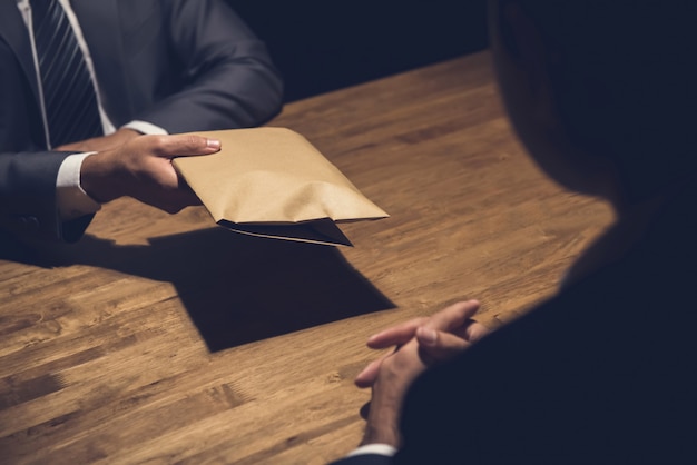 Un hombre dando dinero de soborno en un sobre marrón a otro empresario