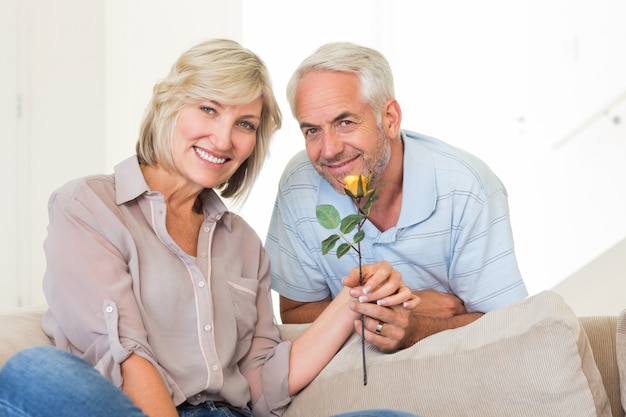 Hombre dando flores a una mujer sonriente sentada en el sofá