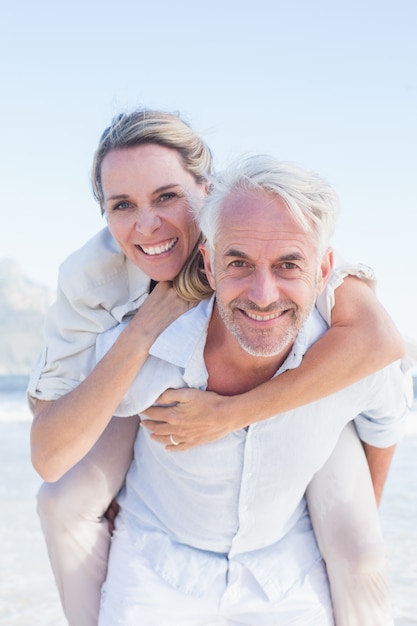 Hombre dando a su esposa sonriente un piggy back en la playa