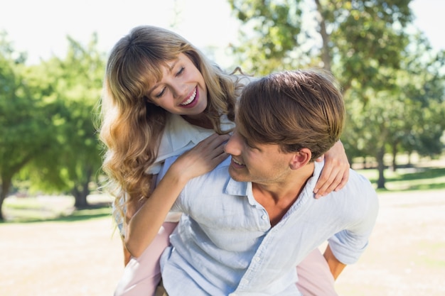 Hombre dando a su linda novia un piggy back en el parque sonriendo el uno al otro