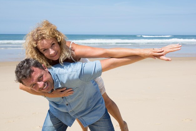 Hombre dando a su linda novia un piggy back en la playa