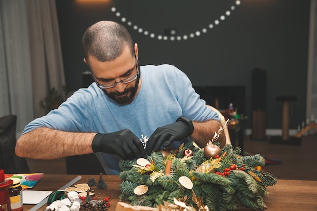 Hombre decorando una corona de Navidad Decoración de corona de árbol de Navidad con taller de bricolaje de mano de hombre