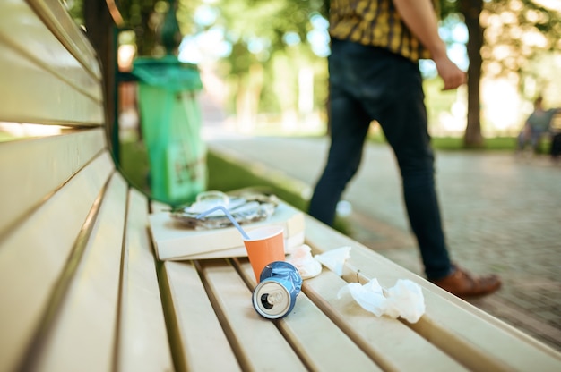 El hombre dejó basura en un banco cerca de un contenedor en el parque, motivador voluntario. Restauración ecológica, estilo de vida ecológico, cuidado de la ecología, concepto de limpieza del medio ambiente