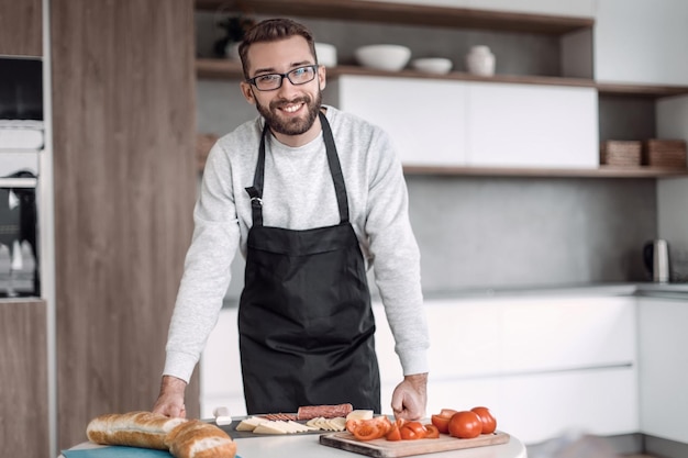 Hombre en un delantal rebanando salami para sándwiches