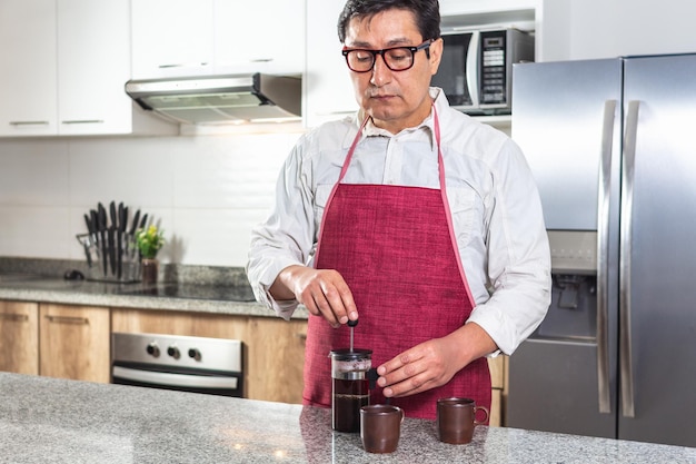 Hombre con delantal rojo preparando café en una prensa francesa en la cocina