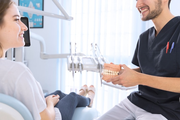 Hombre dentista explicando paciente con modelo de dientes en clínica