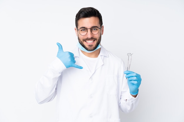 Hombre dentista con herramientas aisladas en pared blanca haciendo gesto de teléfono