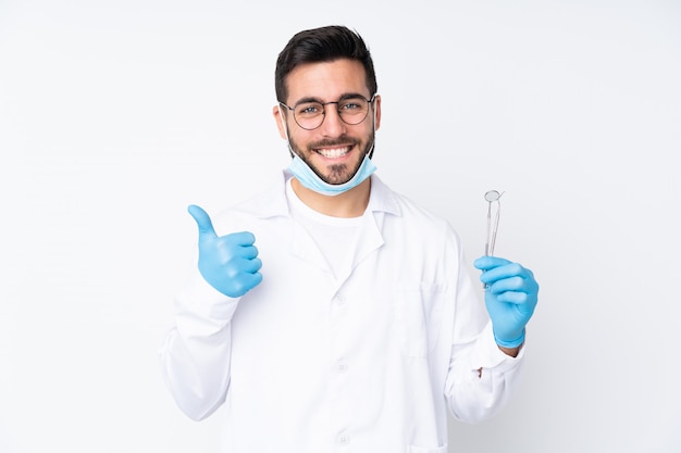 Hombre dentista con herramientas en la pared blanca dando un gesto de pulgares arriba