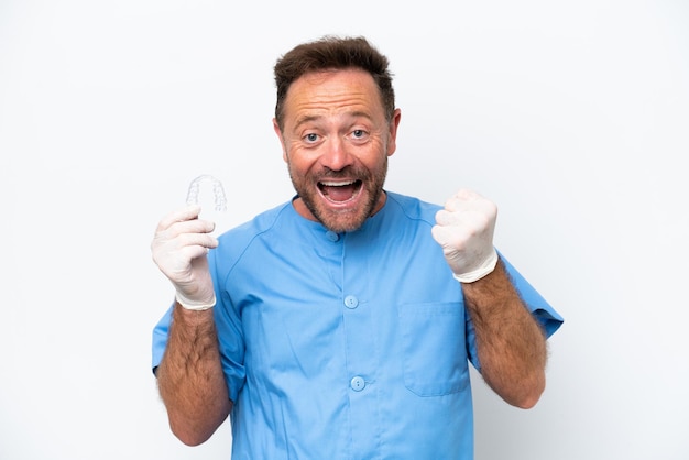 Hombre dentista de mediana edad sosteniendo previendo aislado sobre fondo blanco celebrando una victoria en posición de ganador