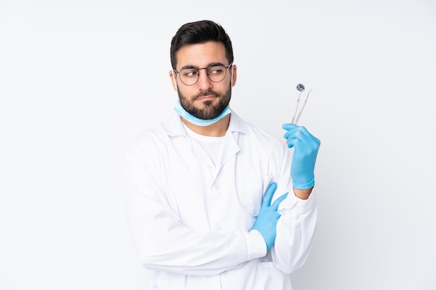 Hombre del dentista que sostiene las herramientas aisladas en la pared blanca que piensa una idea