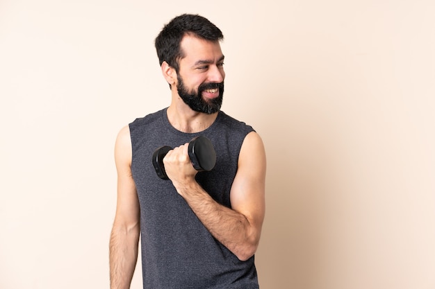 Hombre de deporte caucásico con barba haciendo levantamiento de pesas sobre fondo aislado con los brazos cruzados y feliz