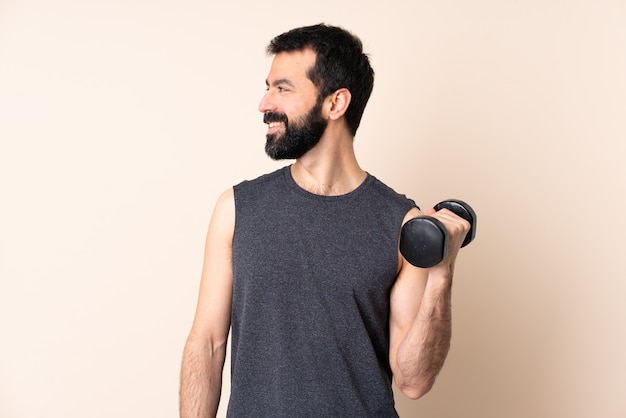 Hombre de deporte caucásico con barba haciendo levantamiento de pesas sobre fondo aislado mirando hacia el lado