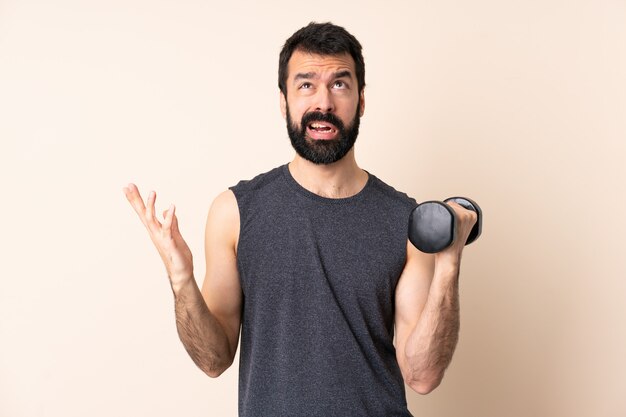 Hombre de deporte caucásico con barba haciendo levantamiento de pesas sobre la pared estresado abrumado