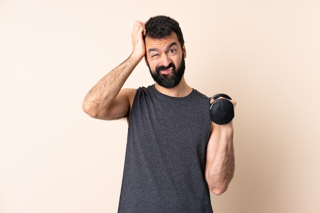 Hombre de deporte caucásico con barba haciendo levantamiento de pesas sobre la pared con una expresión de frustración y no comprensión