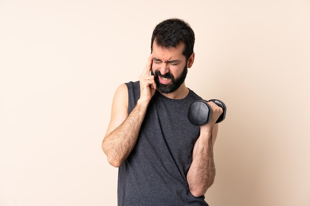 Hombre de deporte caucásico con barba haciendo pesas sobre pared aislada con dolor de cabeza