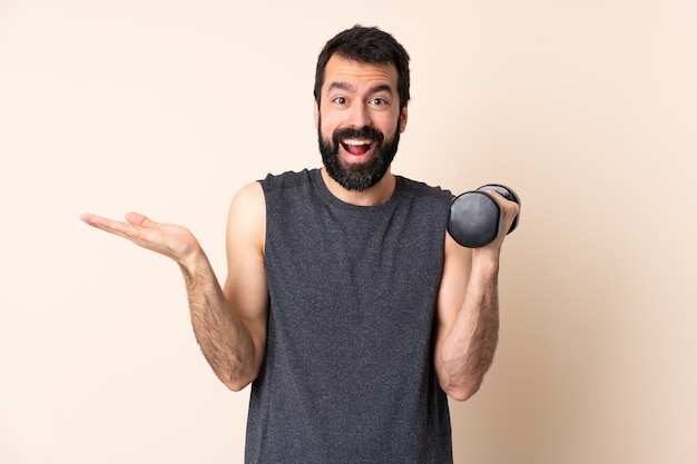 Hombre de deporte caucásico con barba haciendo pesas sobre pared aislada con expresión facial conmocionada