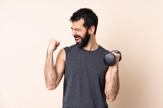 Hombre de deporte caucásico con barba haciendo pesas sobre pared celebrando una victoria