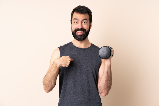 Hombre de deporte caucásico con barba haciendo pesas sobre la pared con expresión facial sorprendida