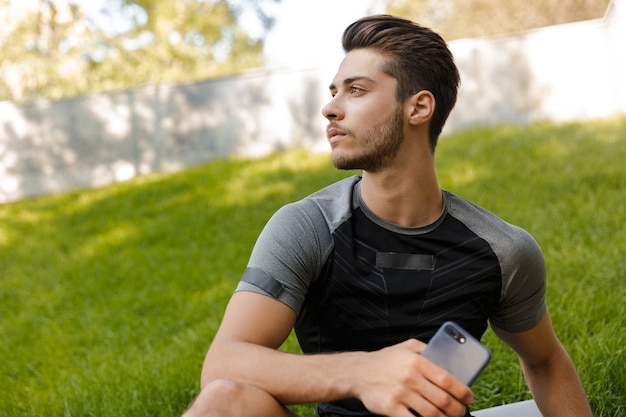 Hombre de deportes concentrados afuera mirando a un lado mediante teléfono móvil