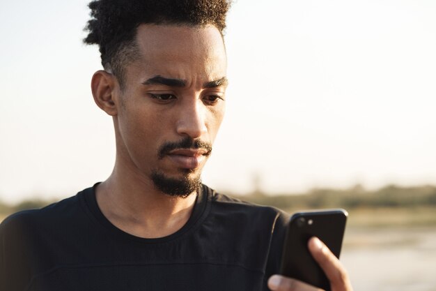 Hombre de deportes fuerte joven guapo con teléfono móvil al aire libre