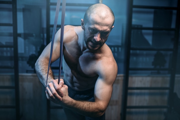 Hombre de deportes musculares con fuertes ejercicios de bíceps con banda elástica en el gimnasio.