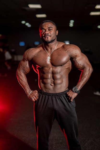 Foto hombre deportista muy musculoso muestra el cuerpo a la cámara. músculos perfectos. fondo oscuro del gimnasio.