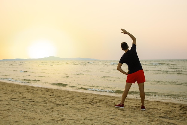 Hombre deportista en ropa deportiva calentamiento entrenamiento hacer ejercicio de estiramiento en arena mar océano playa al aire libre