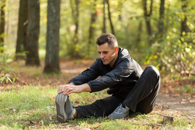Hombre deportivo activo entrena ejercicios de calentamiento o estiramiento en el bosque de otoño Estilo de vida saludable Entrenamiento al aire libre