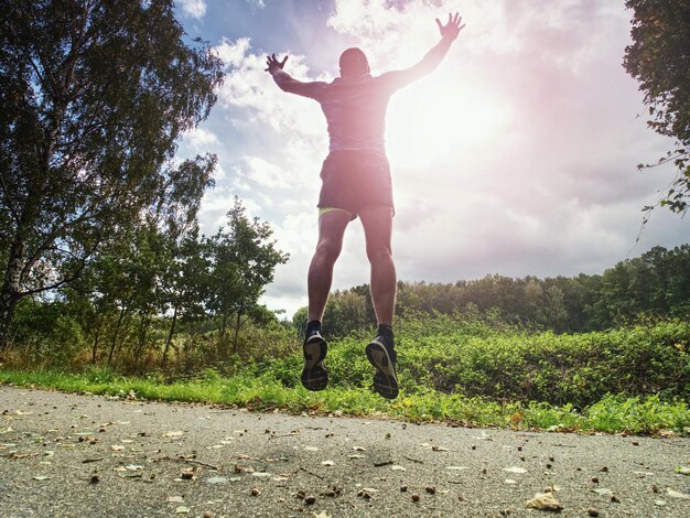 Foto hombre deportivo alto corriendo en las sombras de los árboles con la luz del sol detrás de él mientras lleva pantalones cortos amarillos negros