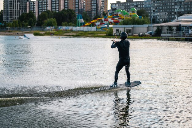 Hombre deportivo balanceándose en wakeboard cabalgando sobre aguas tranquilas del río en un día soleado