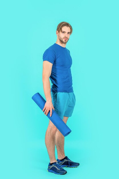 Hombre deportivo con colchoneta de yoga fitness aislado sobre fondo azul